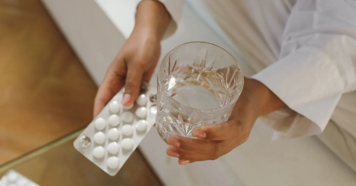 Mãos segurando cápsulas de vitamina e um copo de água