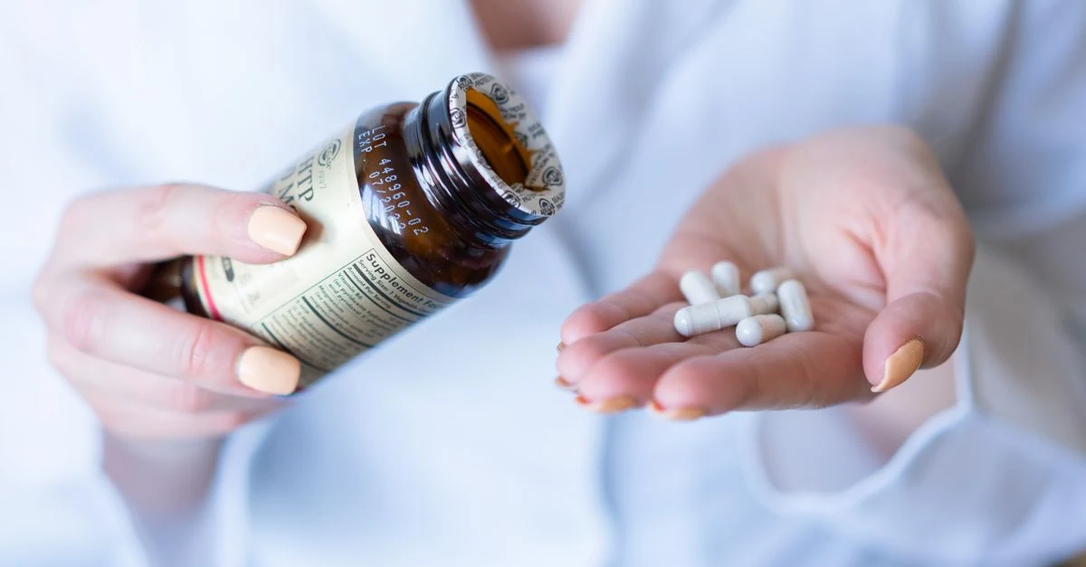 Mão despejando cápsulas de suplemento vitamínico para a palma da outra mão